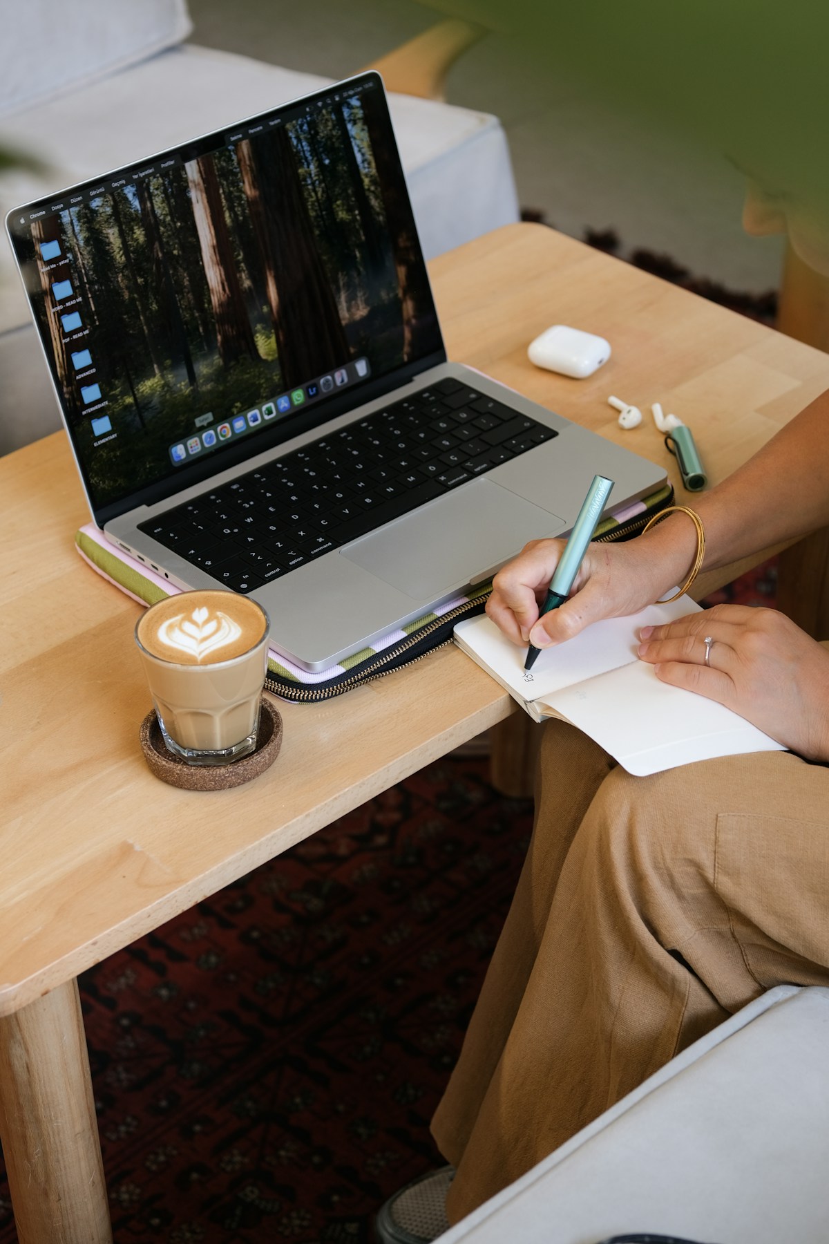Hands writing notes beside a laptop and latte at a wooden café table